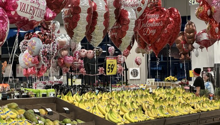photo of interior of grocery store focusing on valentine balloons (red) above bananas (yellow)